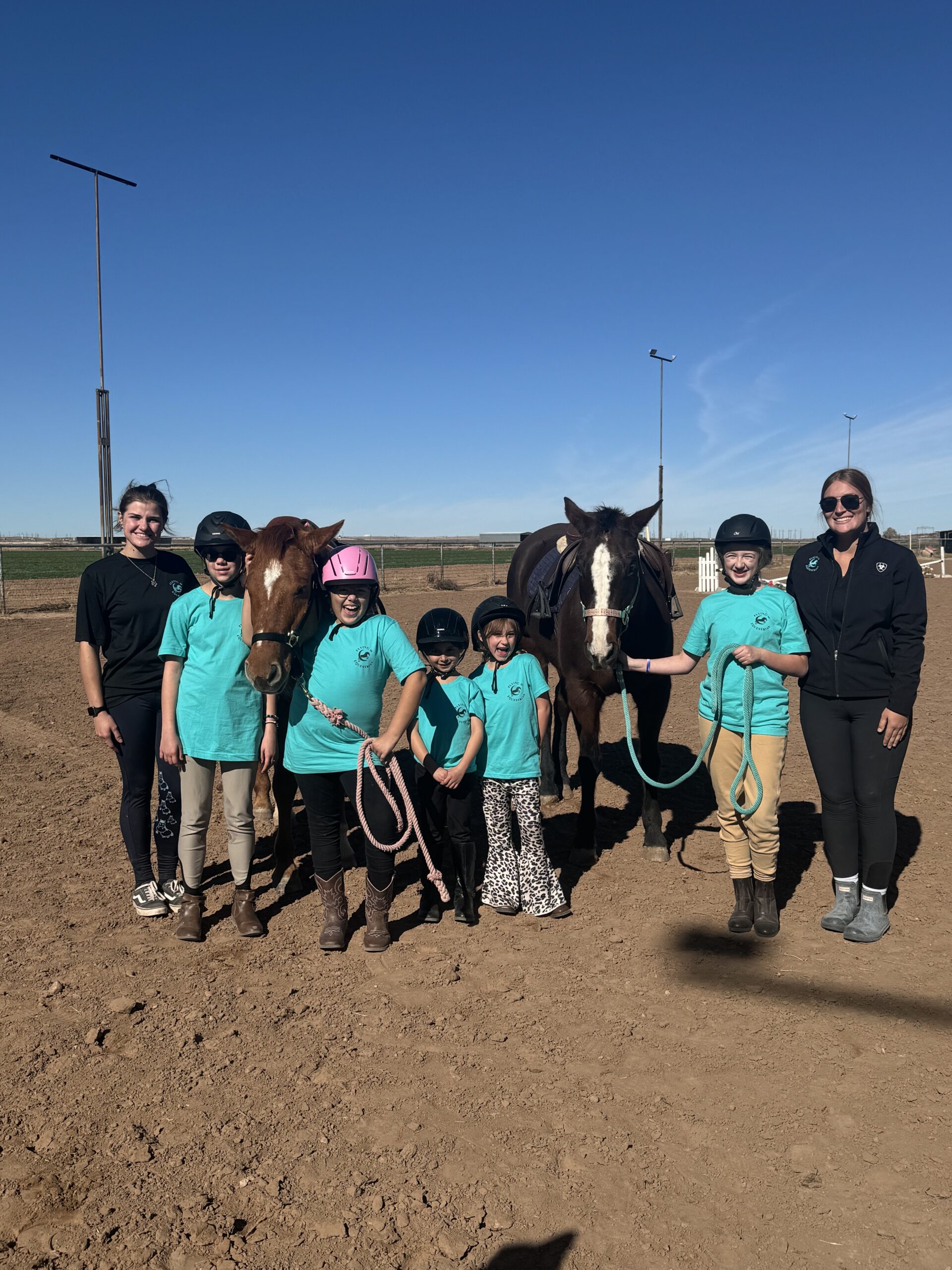 Group of children with horses in an outdoor riding arena wearing matching shirts