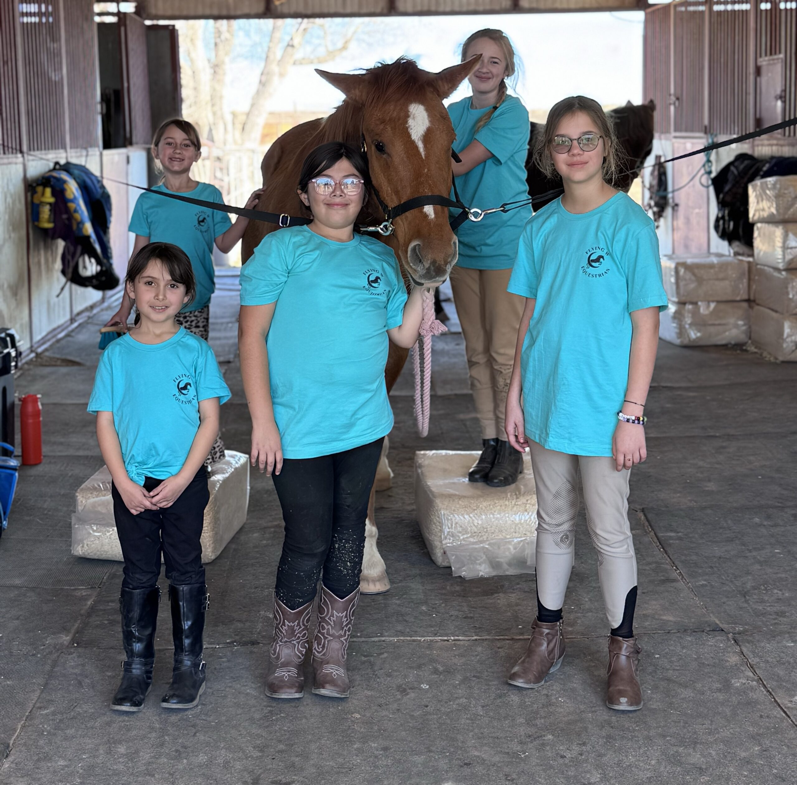Group of children with a horse inside a barn wearing matching shirts